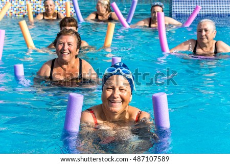 Group of active senior women doing aqua gym in outdoor swimming pool.