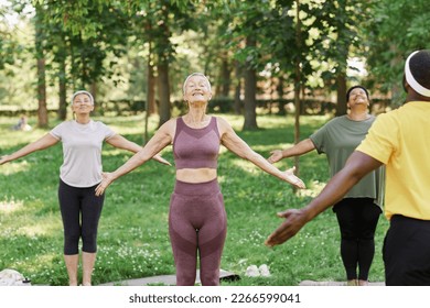 Group of active senior women enjoying yoga outdoors in park and doing breathing exercises
