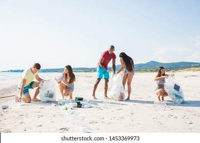 Group Of Activists Friends Collecting Plastic Waste On The Beach. People Cleaning The Beach Up, With Bags. Concept About Environmental Conservation And Ocean Pollution Problems