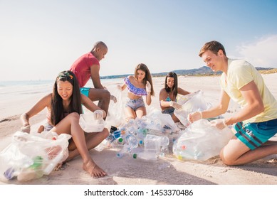 Group Of Activists Friends Collecting Plastic Waste On The Beach. People Cleaning The Beach Up, With Bags. Concept About Environmental Conservation And Ocean Pollution Problems