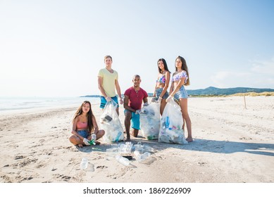 Group Of Activists Friends Collecting Plastic Waste On The Beach. People Cleaning The Beach Up, With Bags. Concept About Environmental Conservation And Ocean Pollution Problems