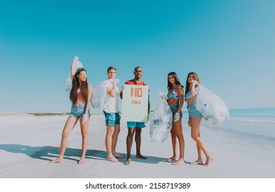 Group Of Activists Friends Collecting Plastic Waste On The Beach. People Cleaning The Beach Up, With Bags. Concept About Environmental Conservation And Ocean Pollution Problems