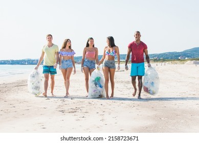 Group Of Activists Friends Collecting Plastic Waste On The Beach. People Cleaning The Beach Up, With Bags. Concept About Environmental Conservation And Ocean Pollution Problems