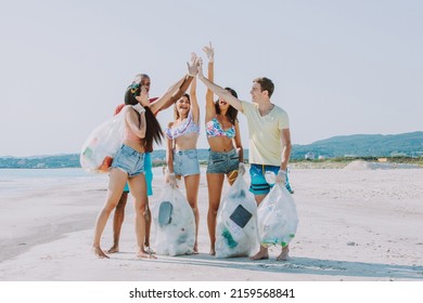 Group Of Activists Friends Collecting Plastic Waste On The Beach. People Cleaning The Beach Up, With Bags. Concept About Environmental Conservation And Ocean Pollution Problems