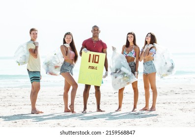 Group Of Activists Friends Collecting Plastic Waste On The Beach. People Cleaning The Beach Up, With Bags. Concept About Environmental Conservation And Ocean Pollution Problems