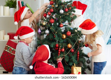 Group Of Adorable Kids In Santa Caps Decorating Xmas Tree