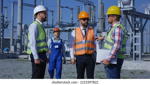 Group of adult diverse men in hardhats gathering on transformer platform of solar electrical plant having discussion