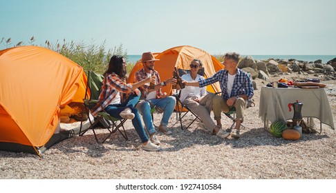 Gruppe erwachsene Freunden entspannen in Kapellenstühlen, trinken Bier und Spaß am Strand zusammen. Reisende toasten Bier und genießen gemeinsam auf dem Campingplatz am Meer. Freundschafts- und Feierlichkeiten.