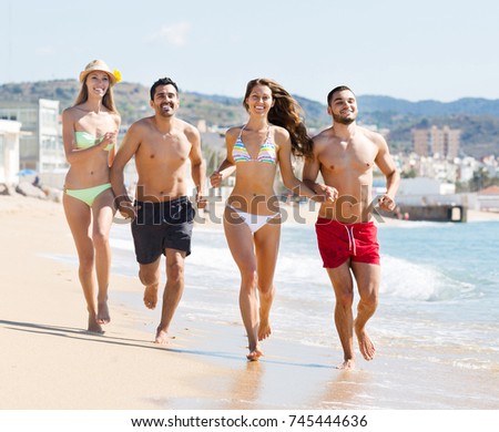 Group of adult russian friends running on sand at beach and smiling

