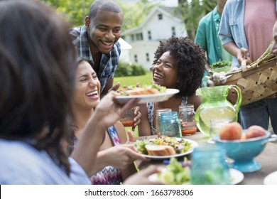 A group of adults and young people at a meal in the garden of a farmhouse. Passing plates and raising glasses.