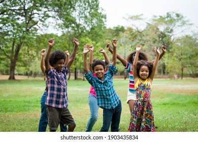 Group of African American children playing and raising their hands in the park. Cheerful diverse black children dancing together outdoor