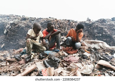 Group of African boys sitting among garbage and plastic waste in an illegal landfill; health risk for street children