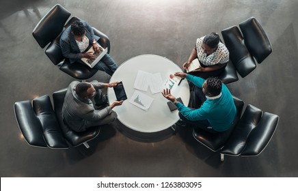 Group Of African Business People Sitting And Discussing Statistics During A Sit Down Meeting Taking From Above