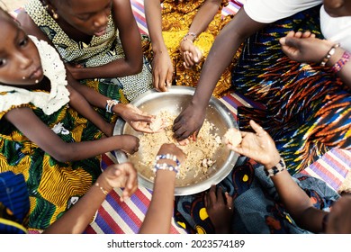 Group Of African Girls Sitting On A Mat, Dividing Their Frugal Meal, Eating With Their Hands From A Large Metal Plate