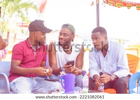group of african guys having interactions outside, table in front of them, one holding smart phone- communication concept 