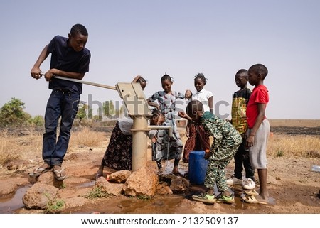 Group of African school age children gathering around a sub saharian village faucet collecting water for their families: Recurrence of World Water Day