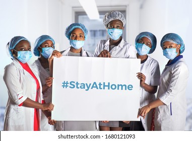 Group of African women nurses activists in face mask, hand sign plackard, caption hashtag StayAtHome. Group of medics, message for social media. Information alert to stay at home to flatten the curve. - Shutterstock ID 1680121093