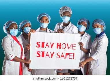 Group Of African Women Nurses Activists In Face Mask With Hand Placard. Text Stay Home Stay Safe. Group Of Medics With Message For Public, Information Alert For Coronavirus Causing Covid-19.