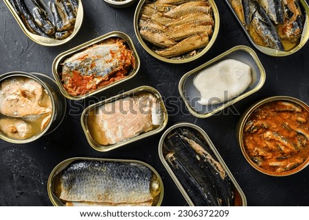 A group of aluminium cans canned with different types of fish and seafood, top view over black textured stone  background.