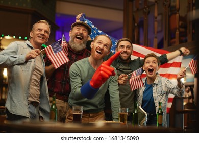 Group of American fans standing at the table with alcohol drinks and watching the game of football team in sport bar - Shutterstock ID 1681345090