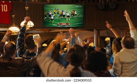 Group of American Football Fans Watching a Live Match Broadcast in a Sports Pub on TV. People Cheering, Supporting Their Team. Crowd Goes Ecstatic When Team Scores a Goal and Wins the Championship.