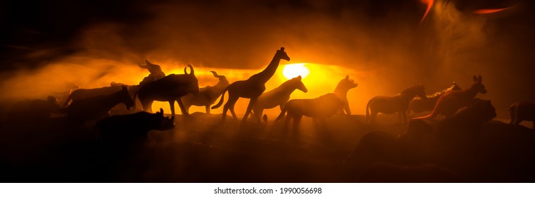 A Group Of Animals Are Grouped Together At Foggy Night With Burning Colorful Background. Animals Running Escaping To Save Their Lives From Fire. Selective Focus.