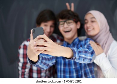 Group Of Arab Teens Taking Selfie Photo On Smart Phone With Black Chalkboard In Background