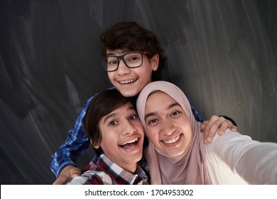 Group Of Arab Teens Taking Selfie Photo On Smart Phone With Black Chalkboard In Background