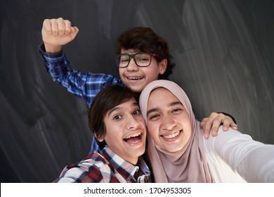 Group Of Arab Teens Taking Selfie Photo On Smart Phone With Black Chalkboard In Background