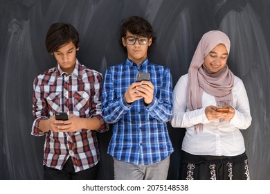 Group Of Arab Teens Taking Selfie Photo On Smart Phone With Black Chalkboard In Background. Selective Focus 