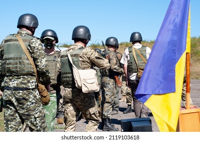 A Group Of Armed Ukrainian Soldiers Near The Flag Of Ukraine. Mobilization. Men In Military Gear With Weapons. Teachings Of The Ukrainian Military. 