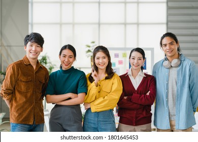 Gruppe asiatischer junger kreativer Menschen in intelligenter, ungezwungener Kleidung lächelnd und Arme in kreativen Büros überquert. Diverse asiatische Männer und Frauen stehen beim Start zusammen. Teamwork-Konzept der Mitarbeiter.