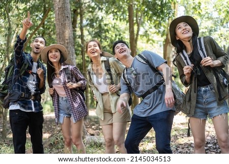 Group of Asian backpacker people have fun travel in forest together. Attractive man and woman friends traveler walking and exploring nature wood with happiness during holiday vacation trip on summer.