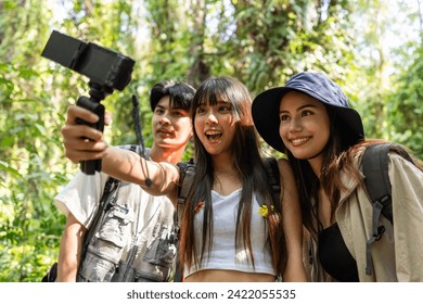 Group of Asian backpacker vlogger have fun travel in forest together. Attractive man and woman friends traveler use camera record video vlog, walk in nature wood with happiness during holiday vacation - Powered by Shutterstock