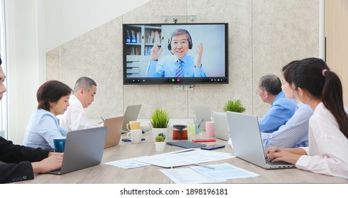 Group Of Asian Business People Having Conference Call Meeting In Boardroom - Old Leader Man Chatting To Colleagues Using Online Video Chat On Tv Screen Discussing Ideas In Office