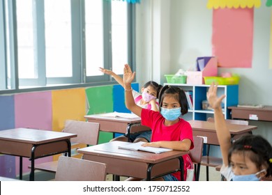 Group Of Asian Children Wearing Protective Mask With Teacher Sitting In Classroom And Raising Hands At Desk In Classroom,Social Distancing,Corona Virus Has Turned Into A Global Emergency.