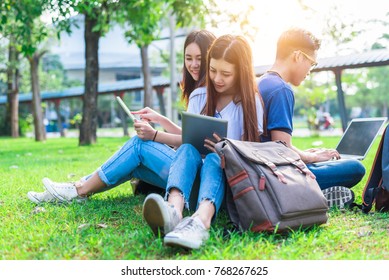 Group Of Asian College Student Using Tablet And Laptop On Grass Field At Outdoors. Technology And Education Learning Concept. Future Technology And Modern Entertainment Concept. Edutainment Theme.