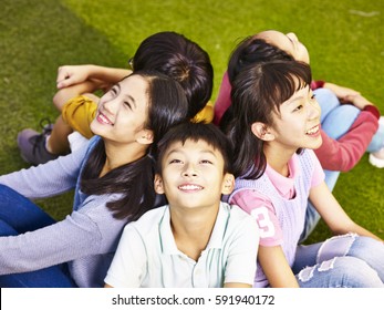 Group Of Asian Elementary School Boys And Girls Sitting On Playground Grass Looking Up At The Sky