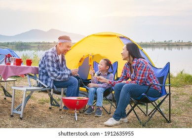 Group of asian family grilling sweet corn and BBQ on stove at camping site, everyone feeling happy. Family outdoor activity concept.