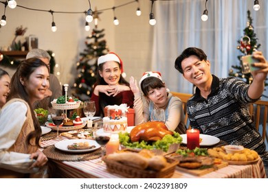 Group of Asian family selfie an enjoying Christmas party or New Year celebrating while father using mobile take a photo on festive dinner table capture in the winter holiday at the warm light home - Powered by Shutterstock