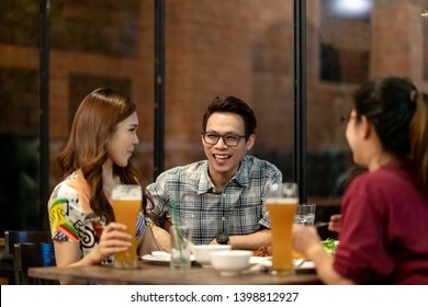 Group Of Asian Friends Hanging Out Talking Together Drink Pint Glass Of Beer On Friday Night In Relaxing After Work TGIF Concept. Attractive Young Asian Join Happy Hour Night Party At Bar Restaurant.