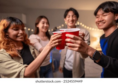 Group of Asian friends having evening party in living room at home. Attractive young man and woman having fun, drinking a red cup of beer to celebrate weekend reunion gathered together in house. - Powered by Shutterstock