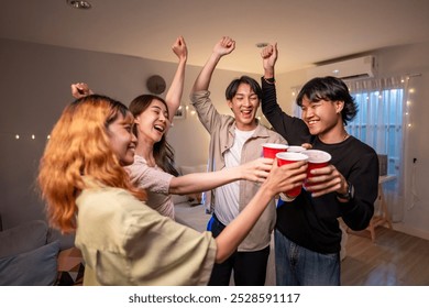 Group of Asian friends having evening party in living room at home. Attractive young man and woman having fun, drinking a red cup of beer to celebrate weekend reunion gathered together in house. - Powered by Shutterstock