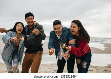 Group of asian friends having fun with sparklers at the beach. Group of young men and women celebrating new year's day at the beach.
