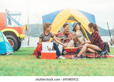 Group Of Asian Friends Having Fun Eating Barbecue Outdoor While Camping And Play Guitar.