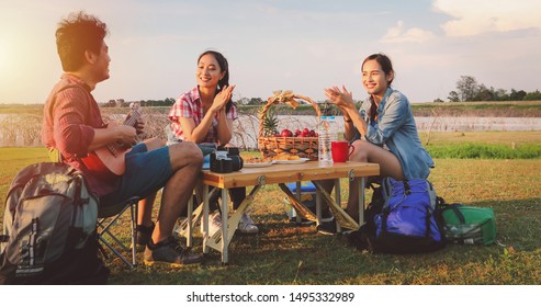 A Group Of Asian Friends Playing Ukelele And Spending Time Making A Picnic In The Summer Holidays.They Are Happy And Have Fun On Holidays.