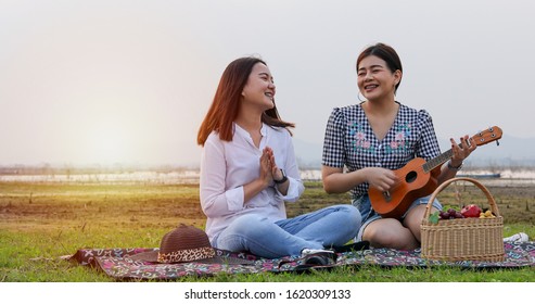 A Group Of Asian Friends Playing Ukelele And Spending Time Making A Picnic In The Summer Holidays.They Are Happy And Have Fun On Holidays.