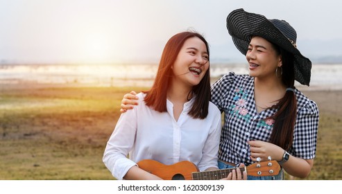 A Group Of Asian Friends Playing Ukelele And Spending Time Making A Picnic In The Summer Holidays.They Are Happy And Have Fun On Holidays.