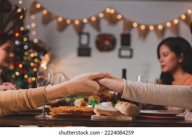 Group of Asian friends praying over Christmas table. Close up of young millennial couple holding hands while praying with friends during Thanksgiving dinner at dining table before saying grace. - Powered by Shutterstock