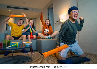 Group Of Asian Friends Sit On Sofa Watching And Cheering Soccer Sports Team On Together TV At Home. Excited Millennial People Sport Fans Celebrate Favorite Football Team Victory In National Match